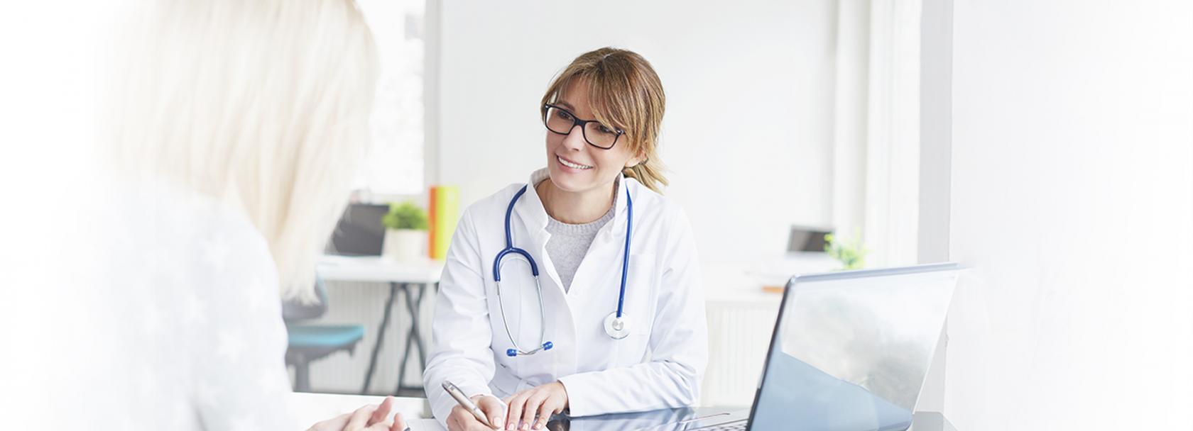 Siedząca lekarka rozmawiająca z pacjentką.