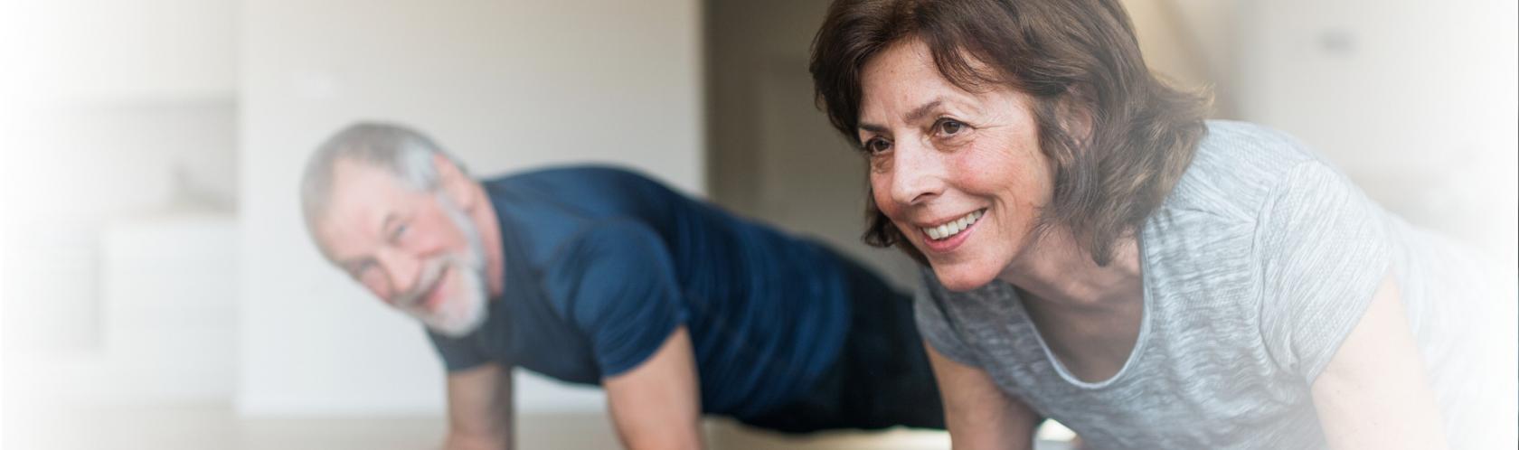 Starsza para ćwiczy w domu, twarzą do podłogi opierają się łokciami na macie