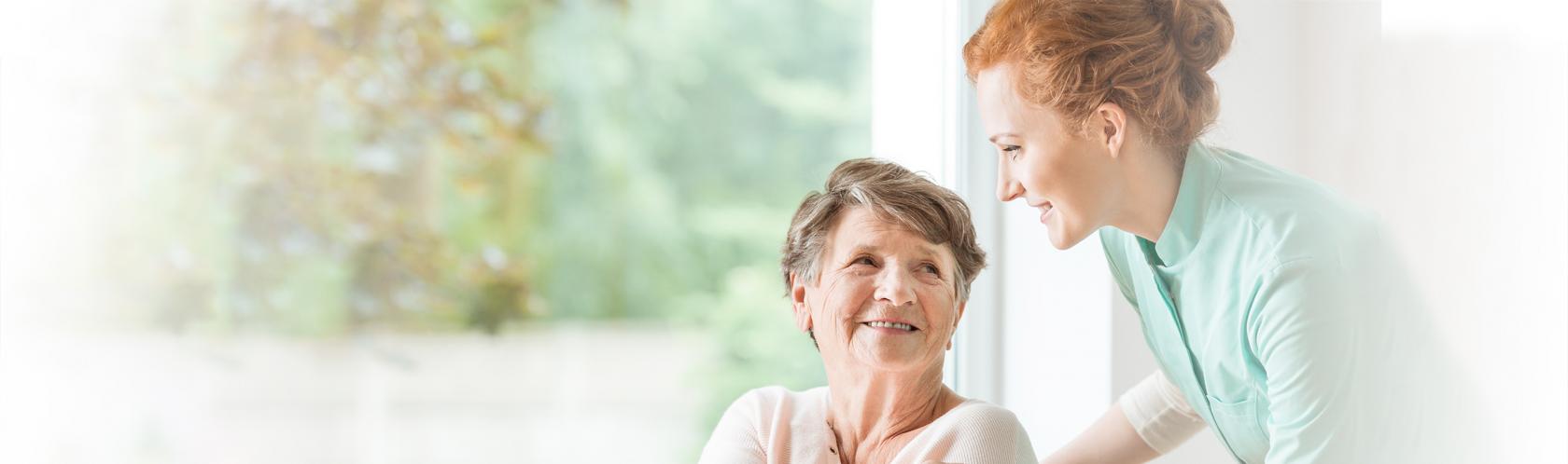 Uśmiechnięta starsza pani na wózku w towarzystwie młodej opiekunki