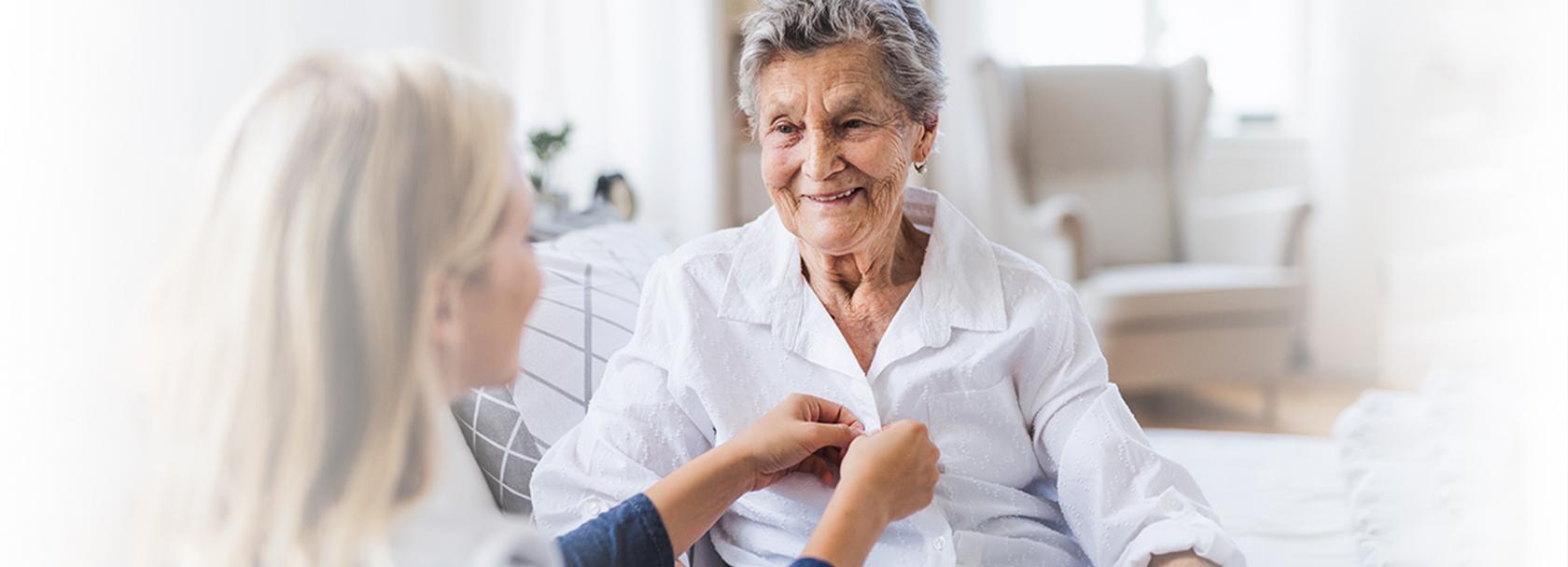 Młoda osoba pomaga się ubrać osobie starszej. Zapina guziki w jej koszuli zuli 