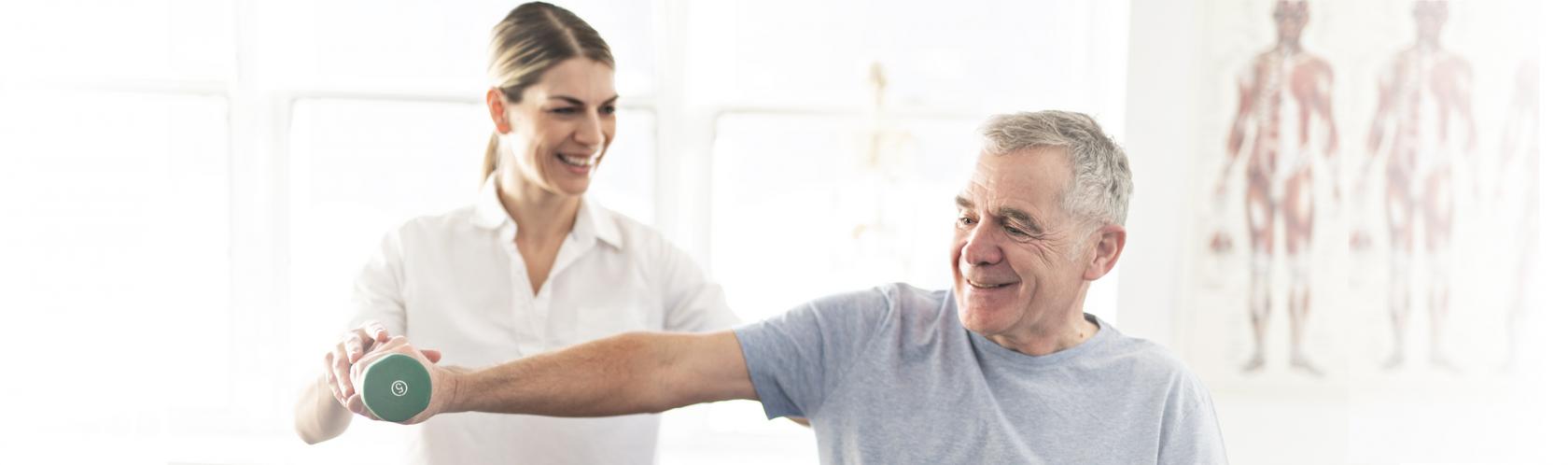 Starszy pan podnosi ciężarek z asystą fizjoterapeutki