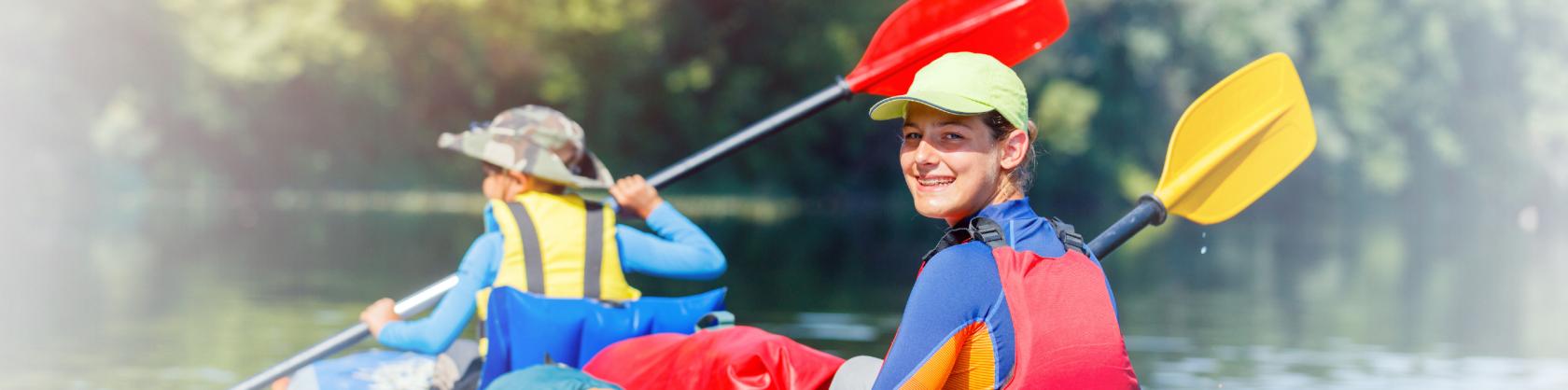 Uśmiechnięte dzieci ubrane w kamizelki ratunkowe płyną na rzece pontonem.