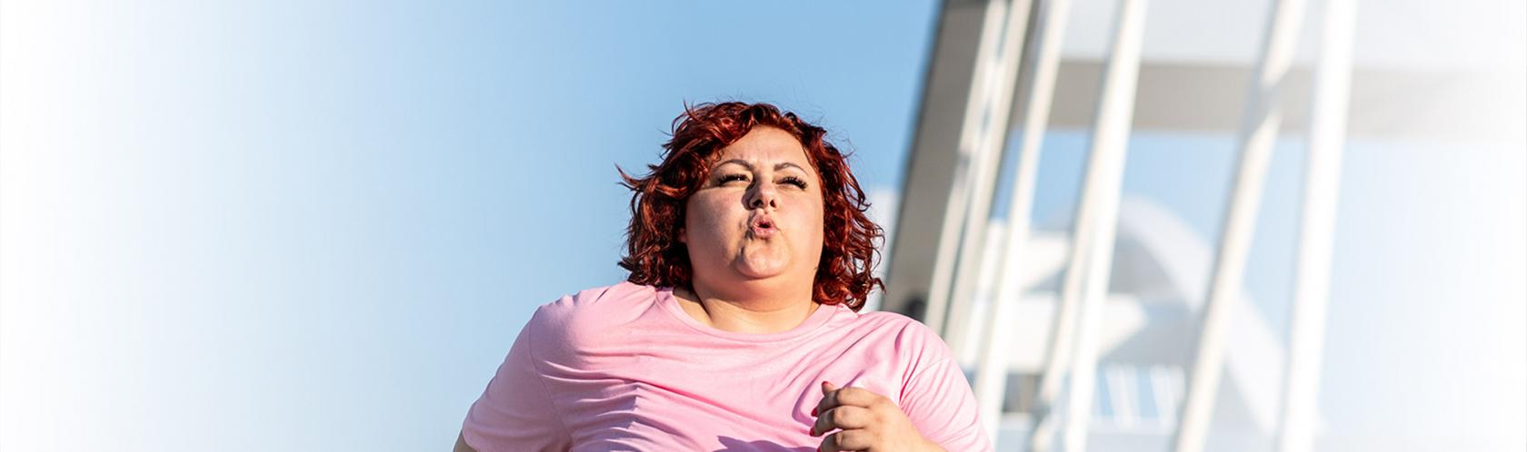 Biegnąca kobieta z nadwagą. W tle nowoczesny most