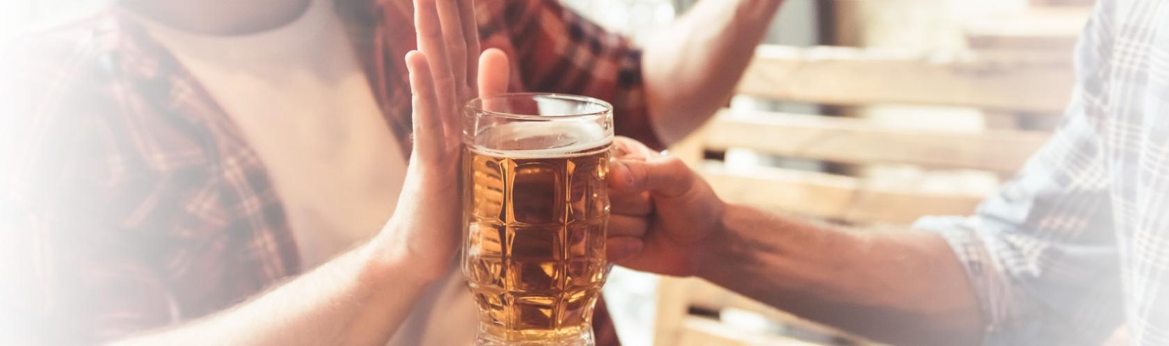 Mężczyzna podaje kufel z piwem koledze, ten odmawia dłonią blokując kufel.