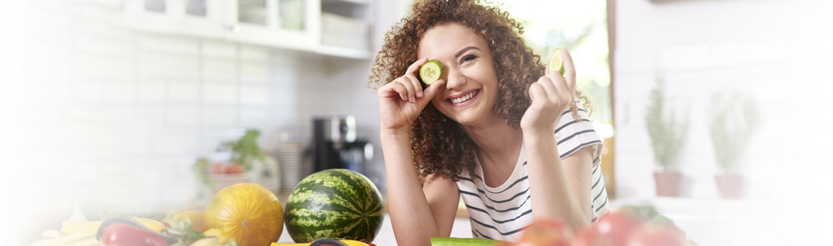 Uśmiechnięta dziewczyna nachylona nad blatem, na którym leżą świeże warzywa.