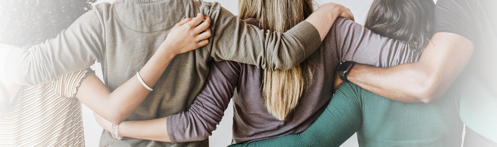 Cztery osoby stoją tyłem i obejmują się ramionami.