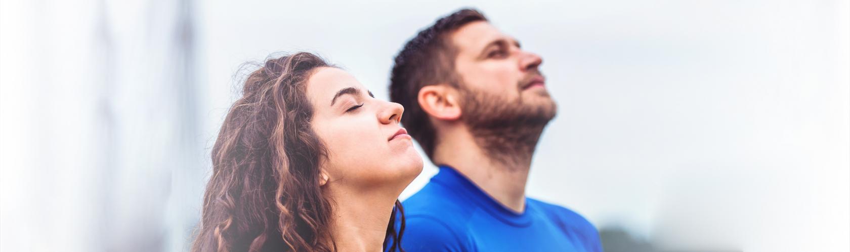 Młodzi kobieta i mężczyzna stoją z głowami skierowanymi ku niebu i oddychają pełną piersią świeżym powietrzem.