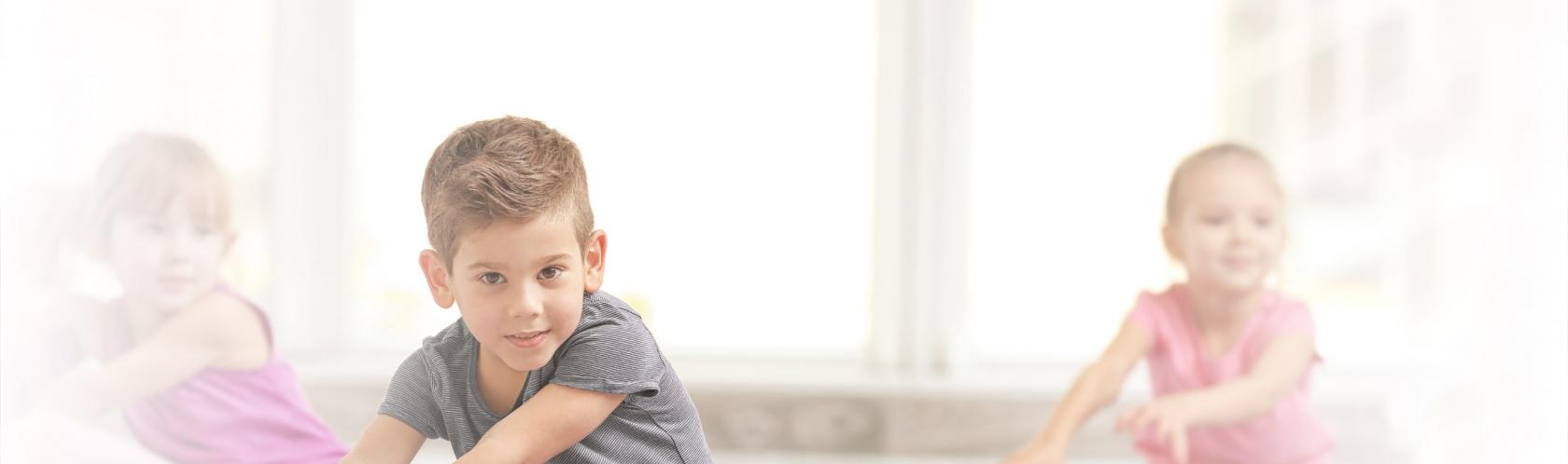 Dzieci na sali gimnastycznej rozciągające nogi w siadzie.