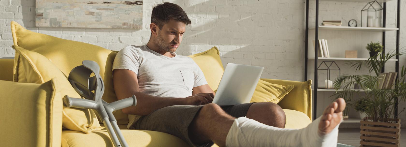 Mężczyzna z nogą w gipsie z komputerem na kolanach