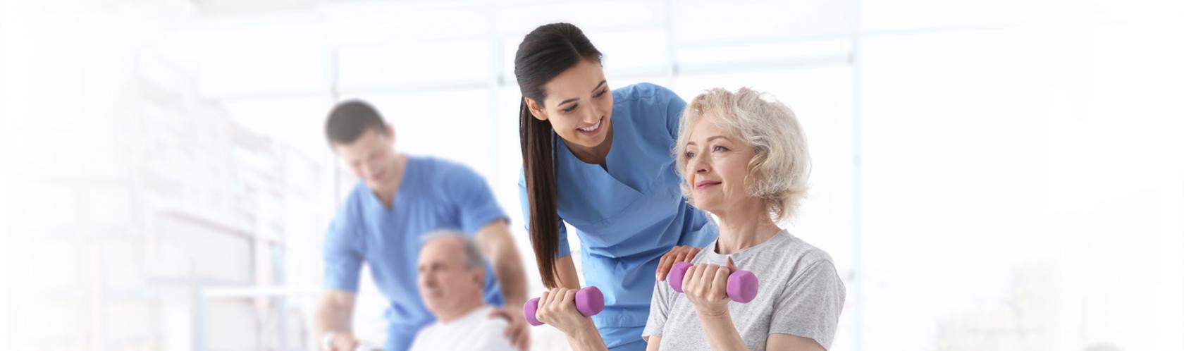 2 osoby ćwiczące na piłce i z cieżarkami na sali gimnastycznej pod ohiem rehabilitanta