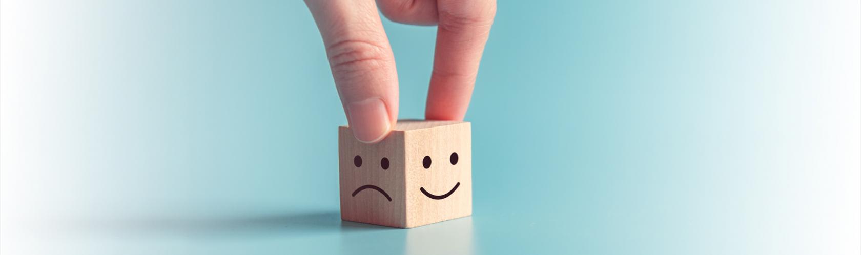 Drweniana kostka, na jednej ściance jest smutna buźka, na drugiej uśmiechnięta.