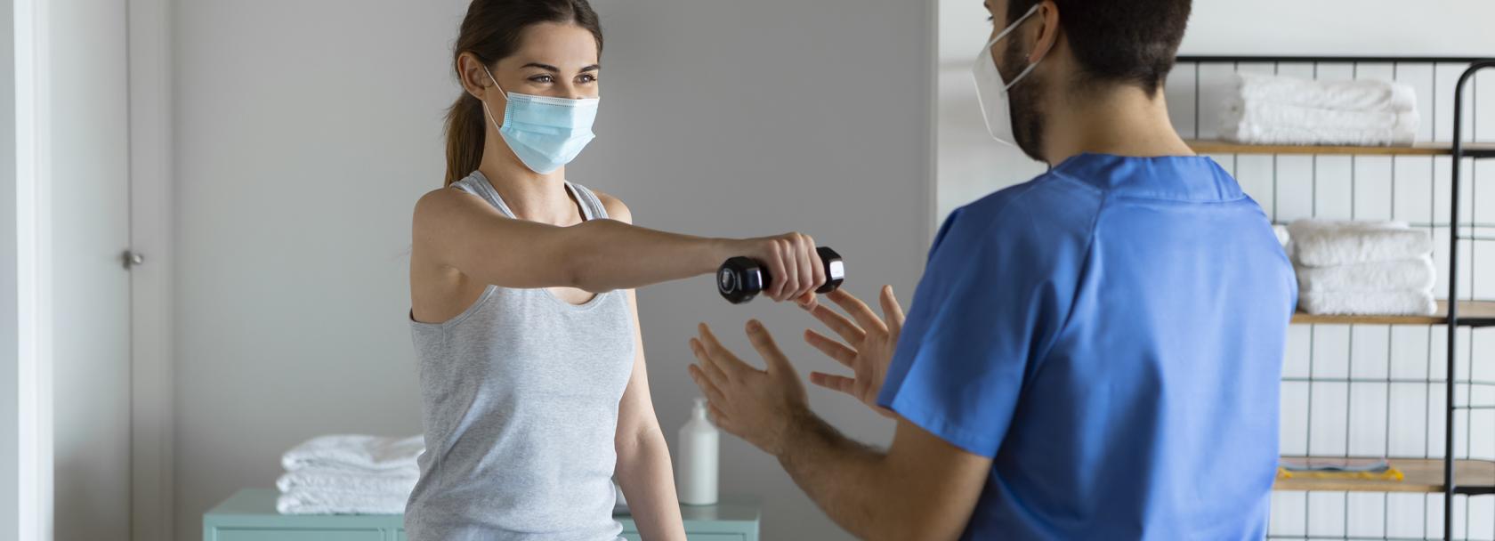 Młoda kobieta w maseczce ćwiczy z rehabilitantem