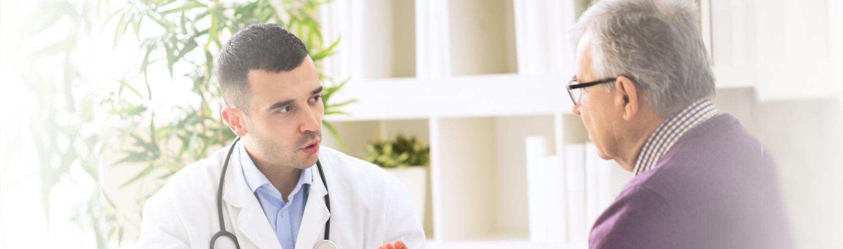 Siedzą lekarz i bokiem starszy pan. Lekarz coś tłumaczy