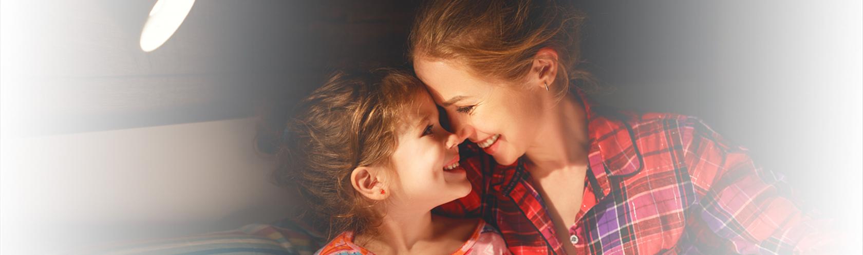 Uśmiechnięte młoda matka i córka w wieku wczesnoszkolnym. Siedzą i wspólnie czytają książkę.