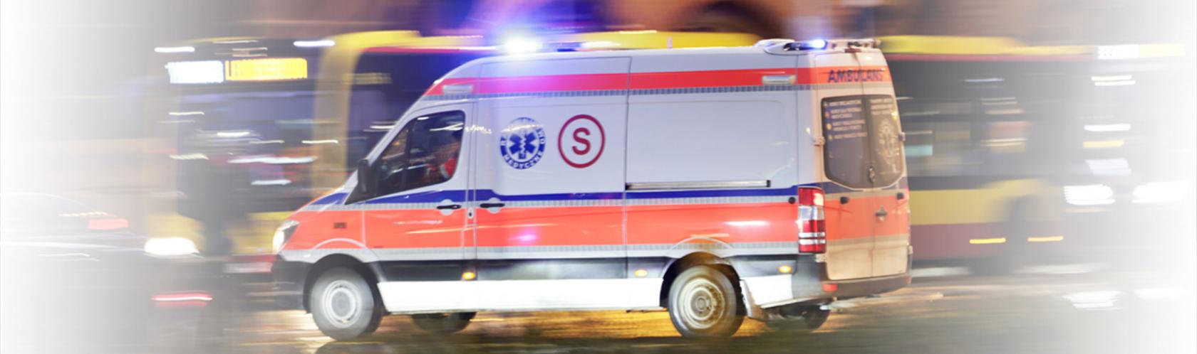 Karetka na sygnale jedzie ulicą w nocy. 