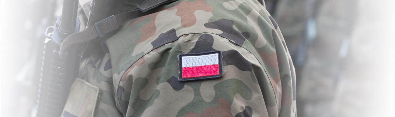 Fragment salutującego żołnierza w mundurze z naszywką w polskich barwach