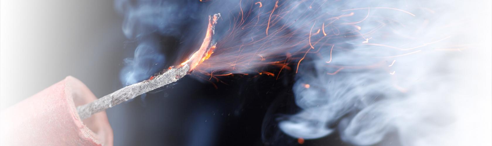 Palący się lont petardy. W tle dużo dymu