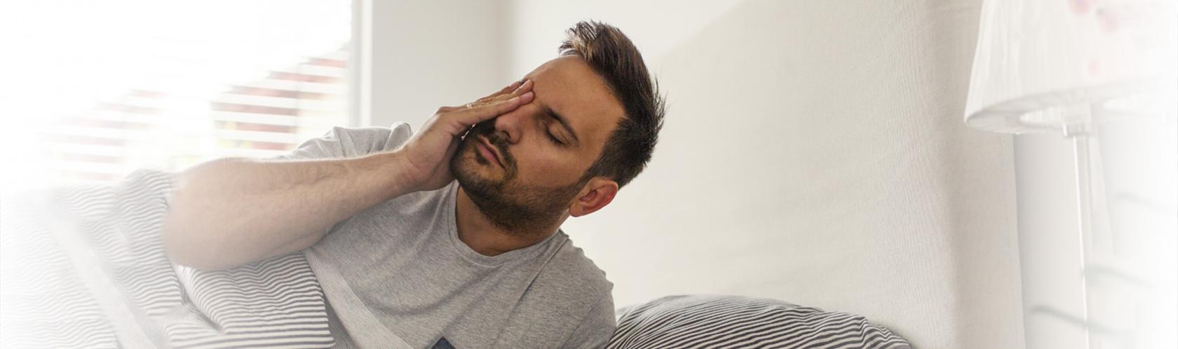 Zmęczony, zaspany mężczyzna wstaje z łóżka.