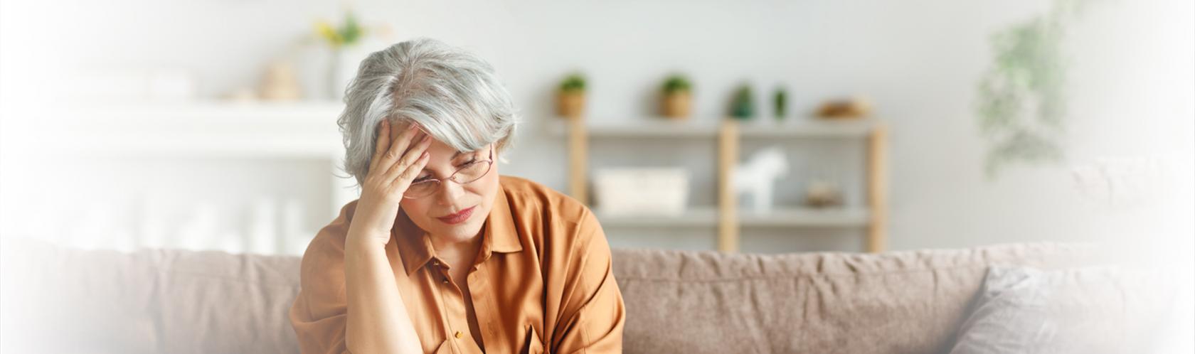 Kobieta na kanapie przed laptopem, podpierająca głowę ręką w geście przytłoczenia