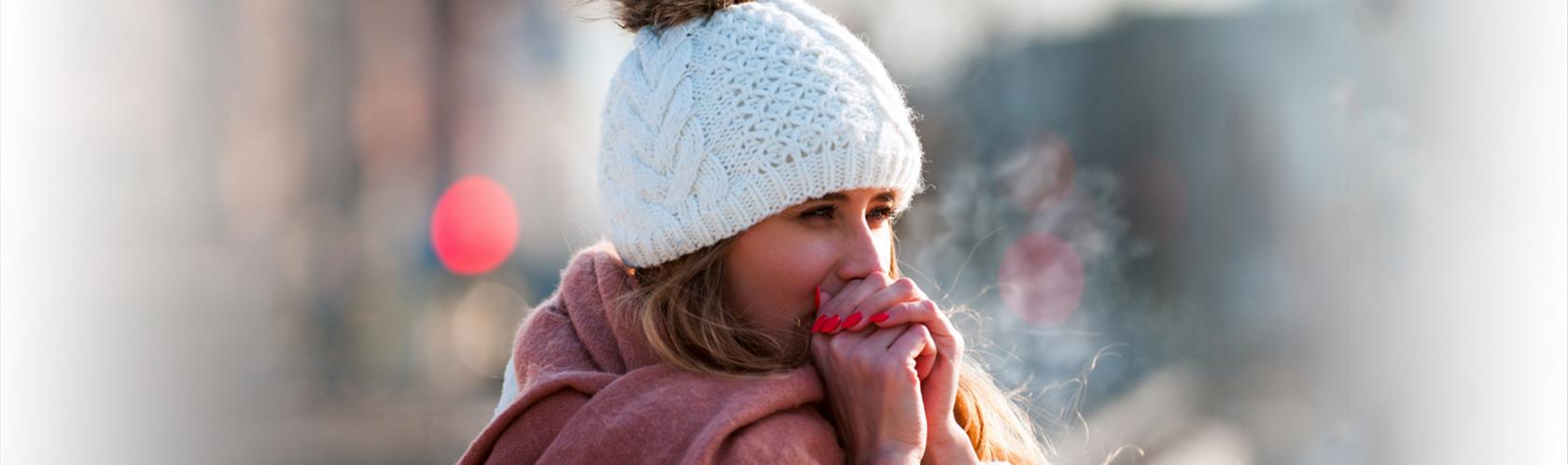 Kobieta w białej czapce, chuchająca w ręce, żeby się rozgrzać