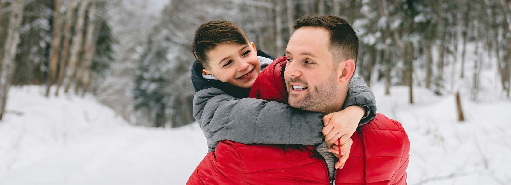 Ojciec niesie syna na barana, są w śnieżnym lesie