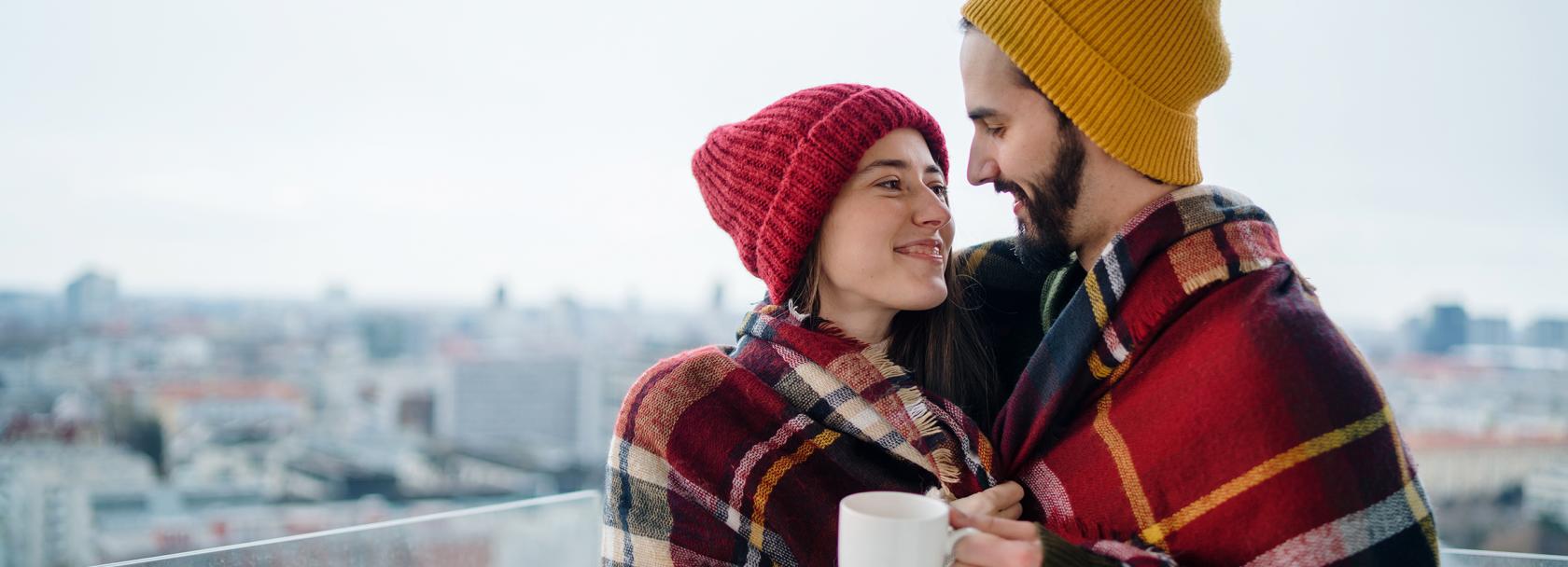 Ona w czerwonej czapce, on w żółtej, na tle mroźnego miasta otulają się kocem