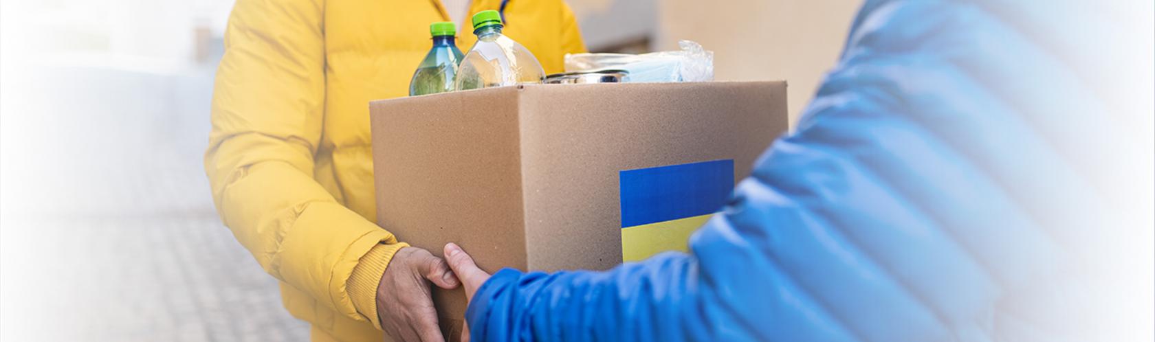 Ktoś przekazuje paczkę z żywnością. Na pudełku jest flaga Ukrainy.