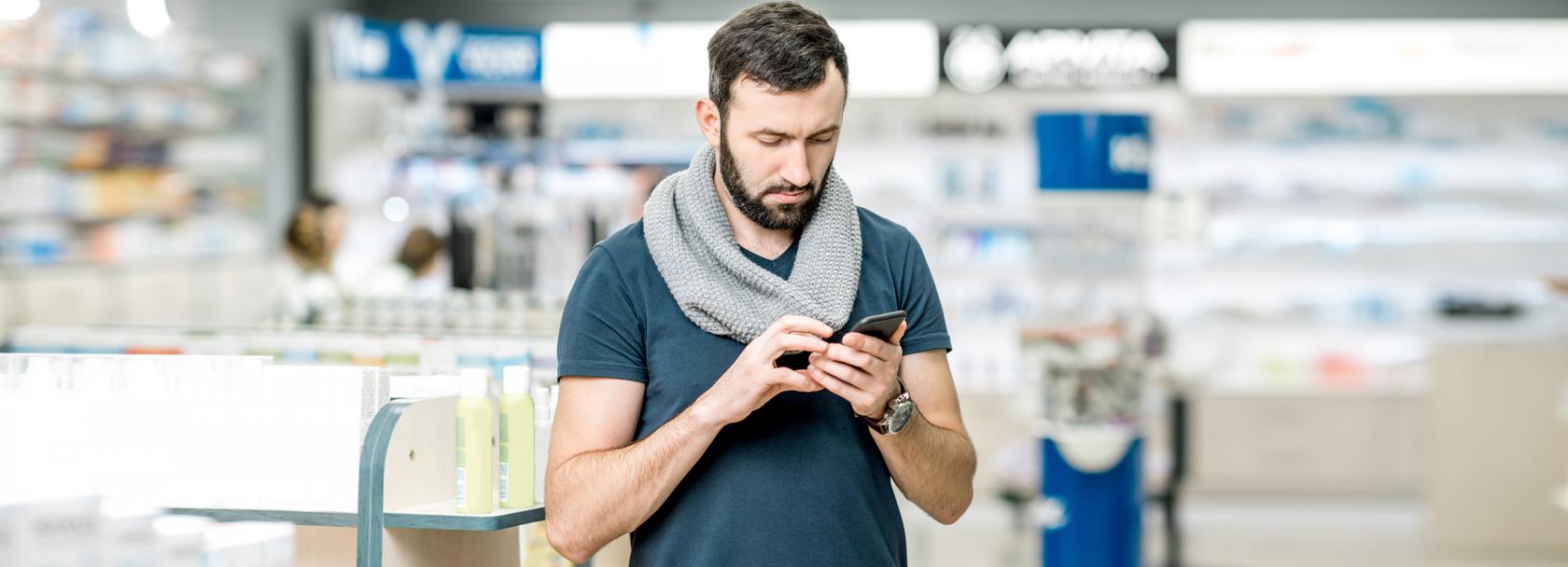 Mężczyzna w aptece patrzy na komórkę