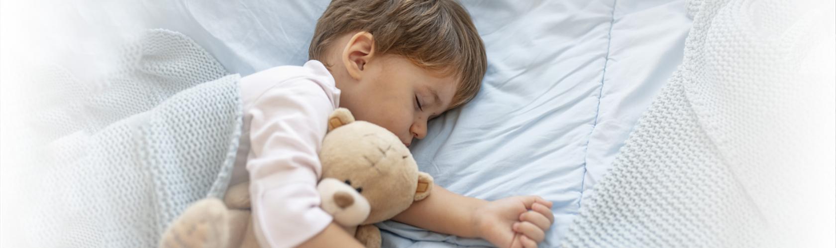 Mały chłopczyk śpi pod kocem. Przytula się do misia.