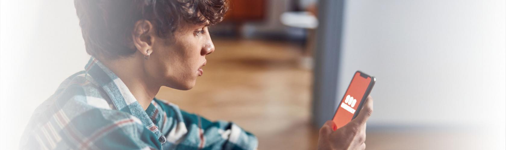 Mlody chłopak trzyma telefon, na którym wyświetla się numer 999. Jest w domu i dzwoni po pomoc.