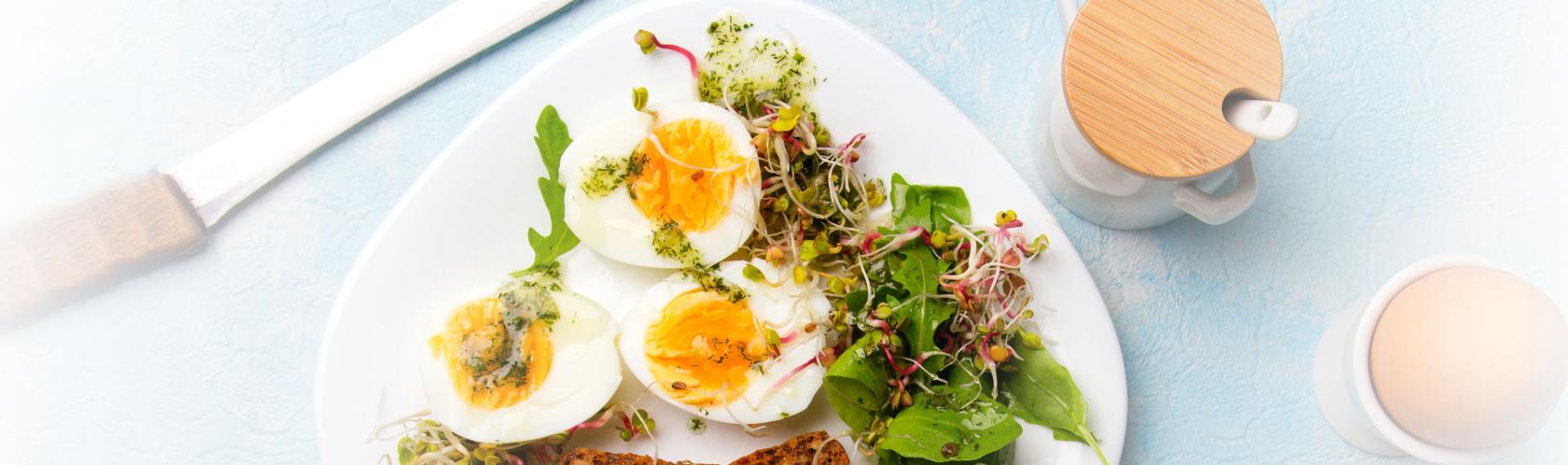 Zdrowe śniadanie. Jajka ugotowane na twardo, świeże kiełki rzodkiewki, rukola z sosem ziołowym i kromki pełnoziarnistego ciemnego chleba.