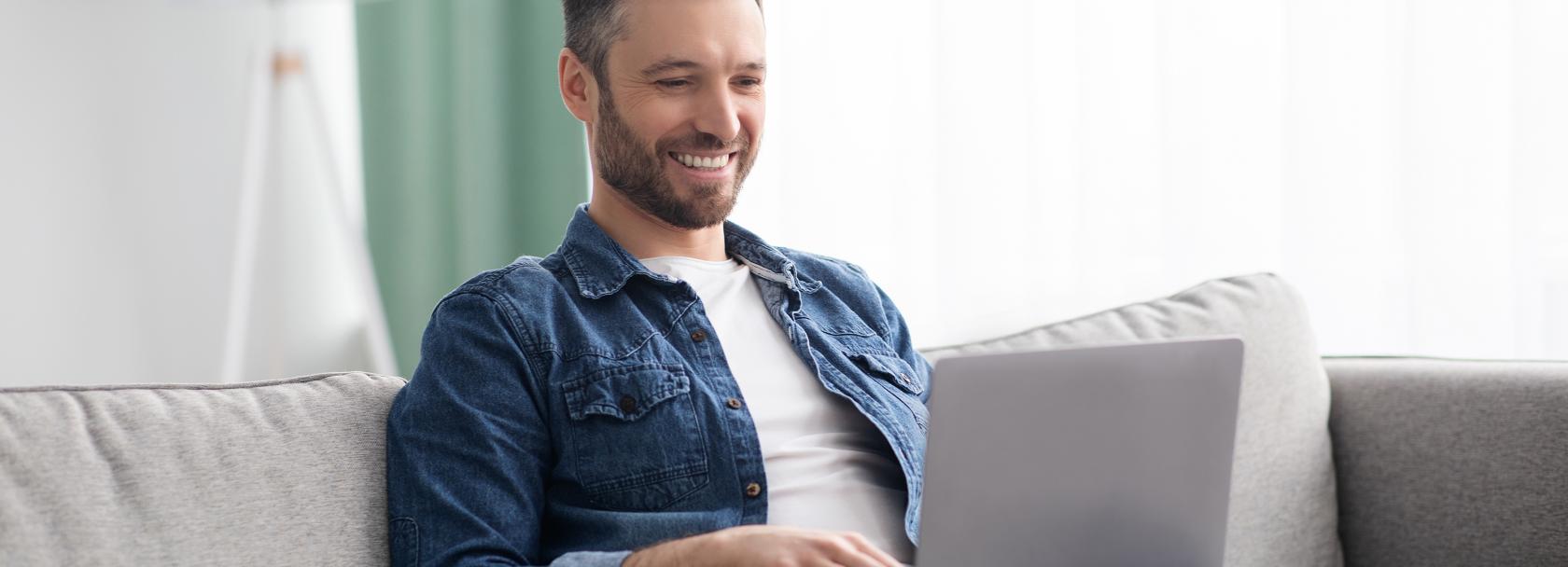 Uśmiechnięty mężczyzna z laptopem na kolanach