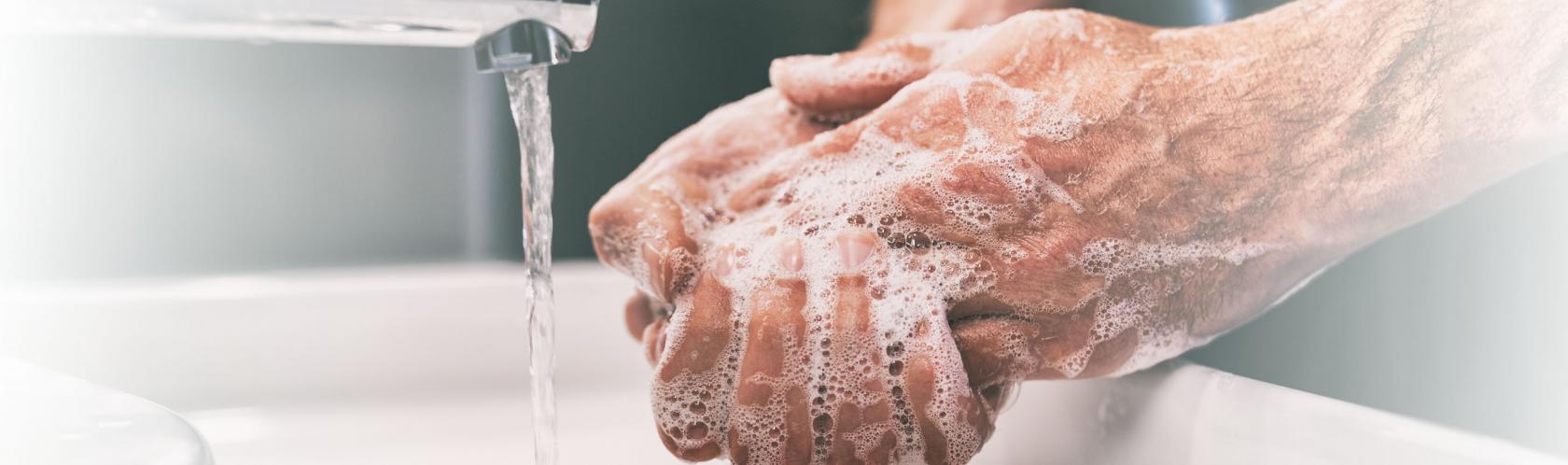 Namydlone dłonie mężczyny nad umywalką podczas mycia rąk.