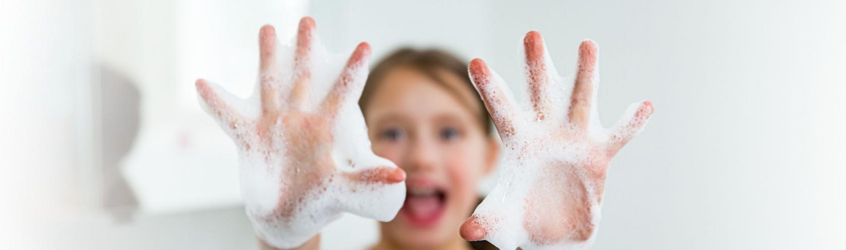 Mała dziewczynka wyciąga ręce do przodu i pokazuje namydlone dłonie.