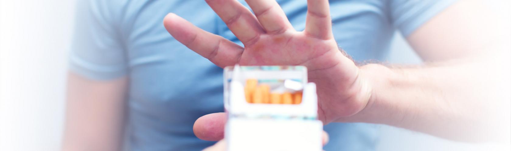 Mężczyzna gestem unisionej dłoni odmawia wzięcia papierosa z pełnej paczki.