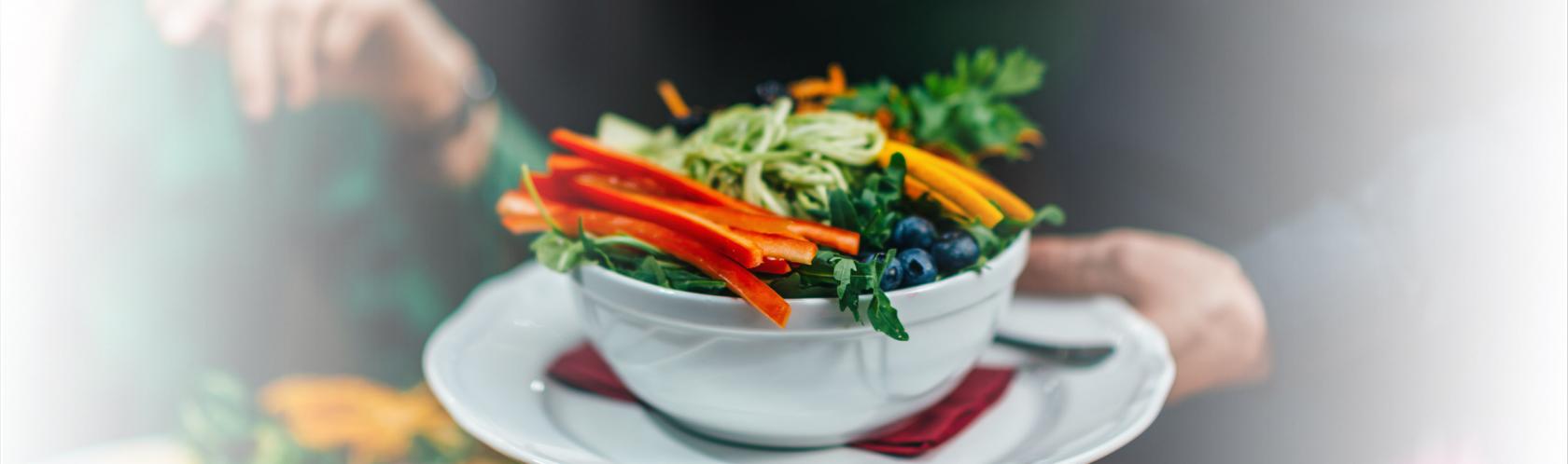 Kelner podaj danie na talerzu. Jest na nim papryka, marchewka, borówka amerykańska, pieruszka, zielony makaron.