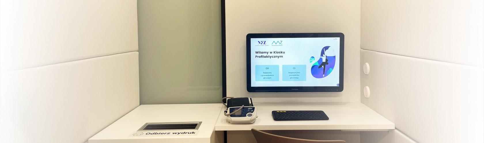 Widok wnętrza kiosku profilaktycznego. Ekran z powitanniem, klawiatura i ciśnieniomierz.