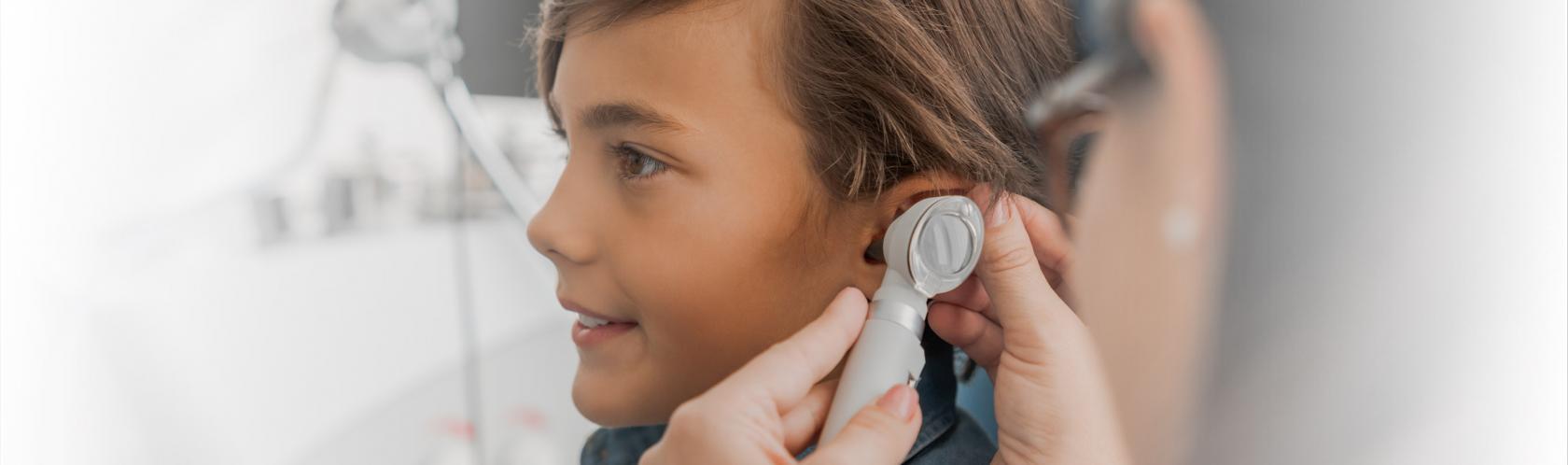 Chłopiec podczas wizyty u laryngologa. Lekarka bada mu ucho otoskopem.