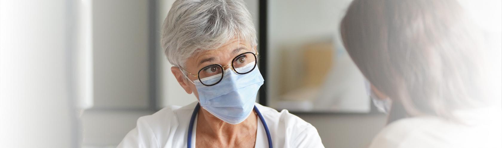 Pacjentka widoczna od tyłu rozmawiająca ze starszą lekarką. Siedzą. Widoczne tyłko górne partie sylwetek.