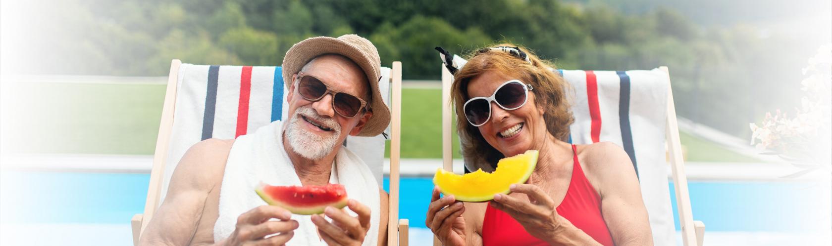 Mężczyzna i kobieta na leżakach, nad basenem. W strojach kąpielowych i okularach przeciwsłownecznych. Jedzą arbuzy. 