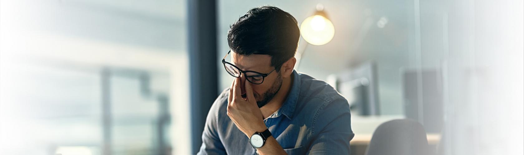 Mężczyna siedzi przed komputerem. Przeciera oczy ze zmęczenia.