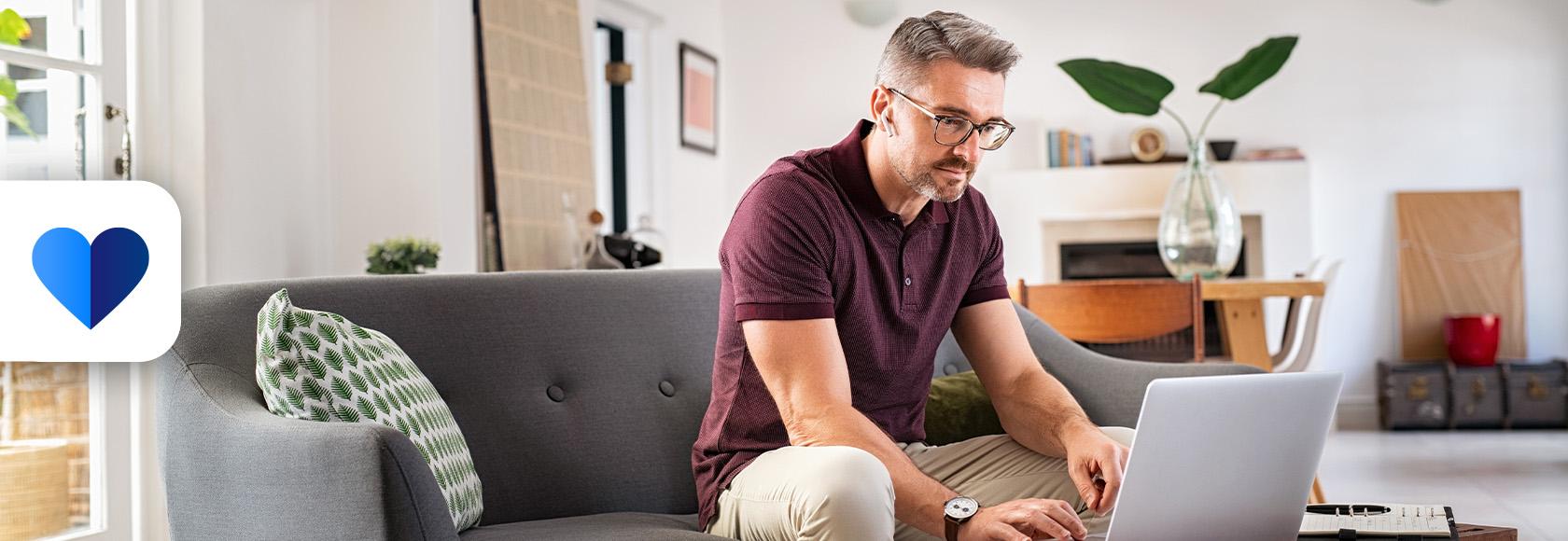 mężczyzna pisze coś w komputerze stojacym na "jamniku" przy kanapie 