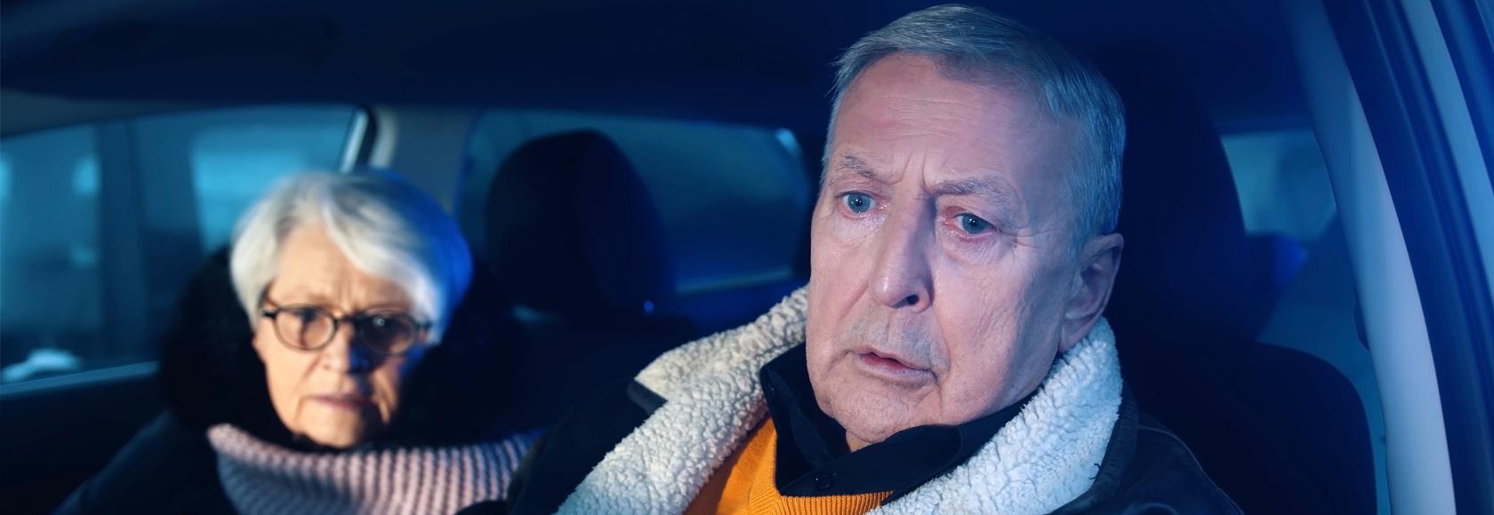 Starsza para w aucie nocą. Mężczyzna za kierownicą jest zmieszany, kobieta lekko wystraszona.