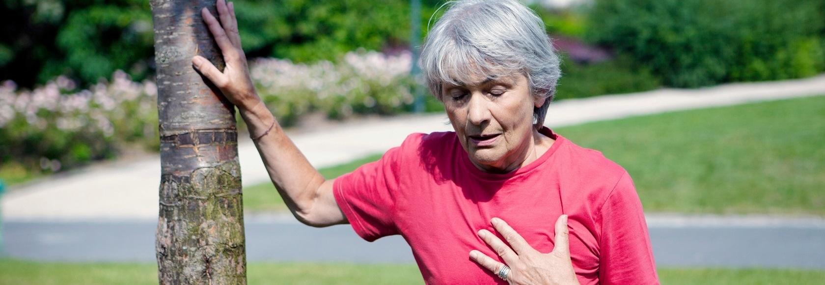 Kobieta trzymająca się ręką za serce, a drugą wspierająca się o drzewo