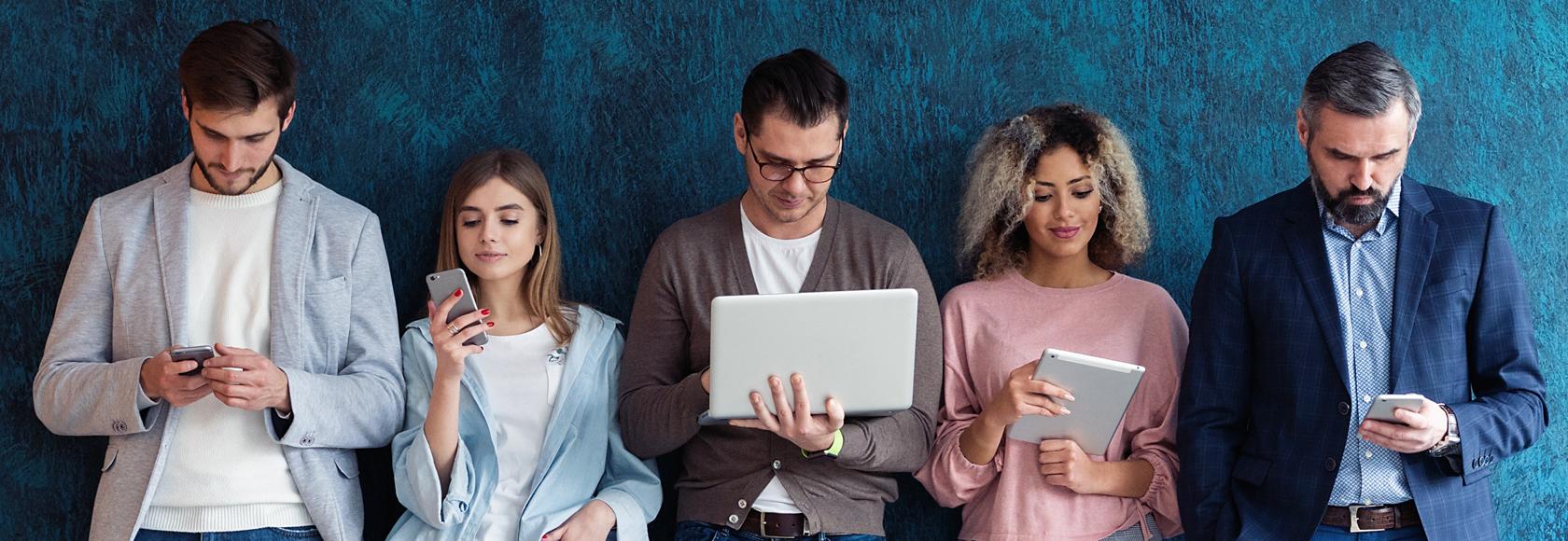 Piatka różnych ludzi stoi przed niebieską ścianą. Trzymają różne urządzenia elektroniczne.