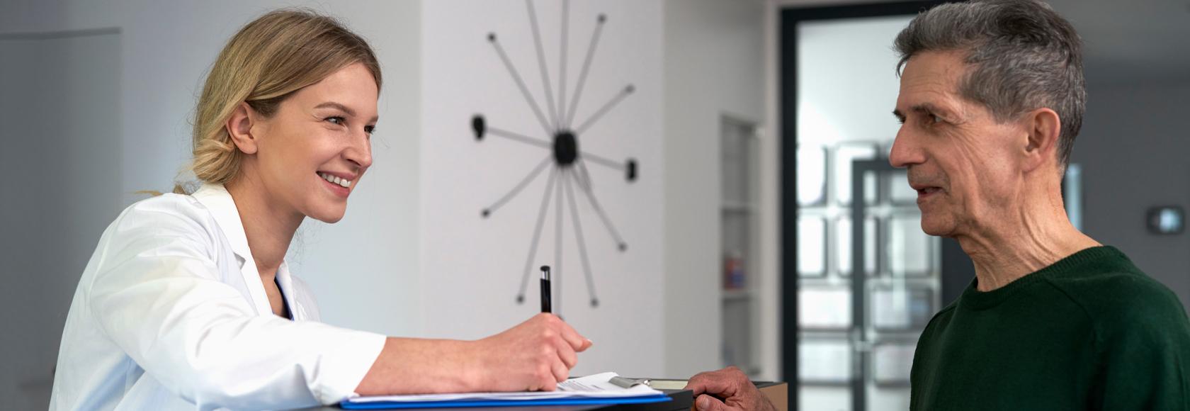 Starszy mężczyzna rozmawia z recepcjonistką w przychodni.
