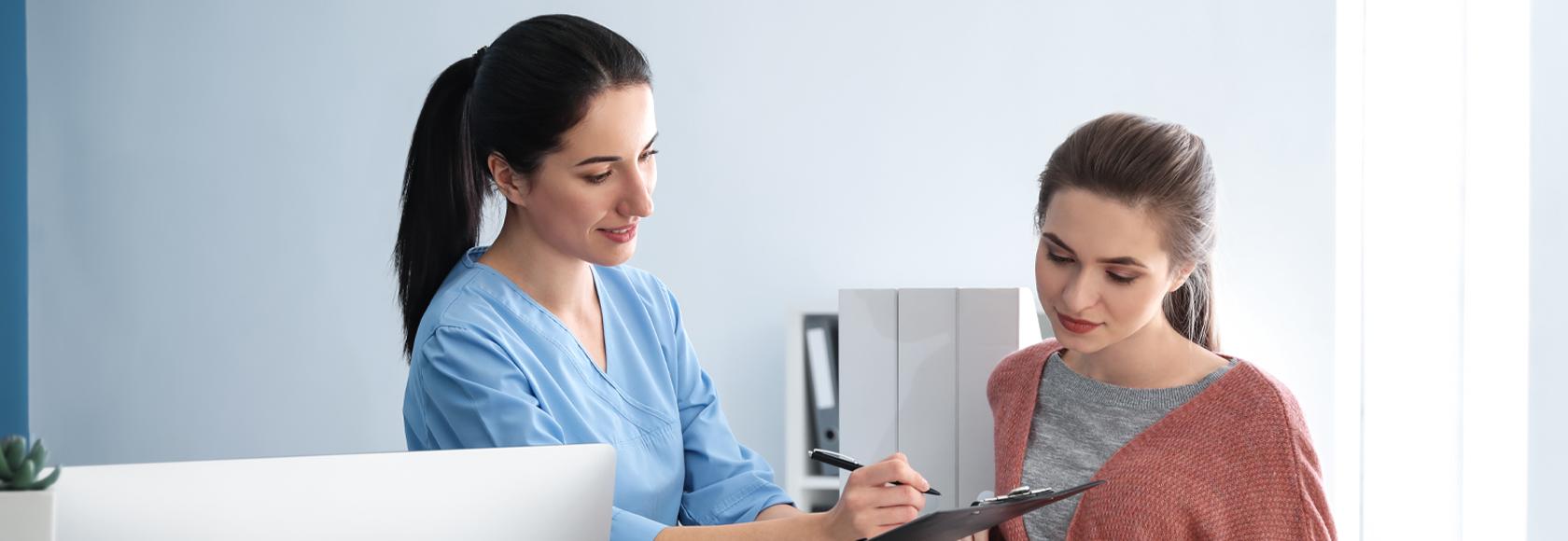 Małoda dziewczyna w przychodni rozmawia z recepcjonistką. 