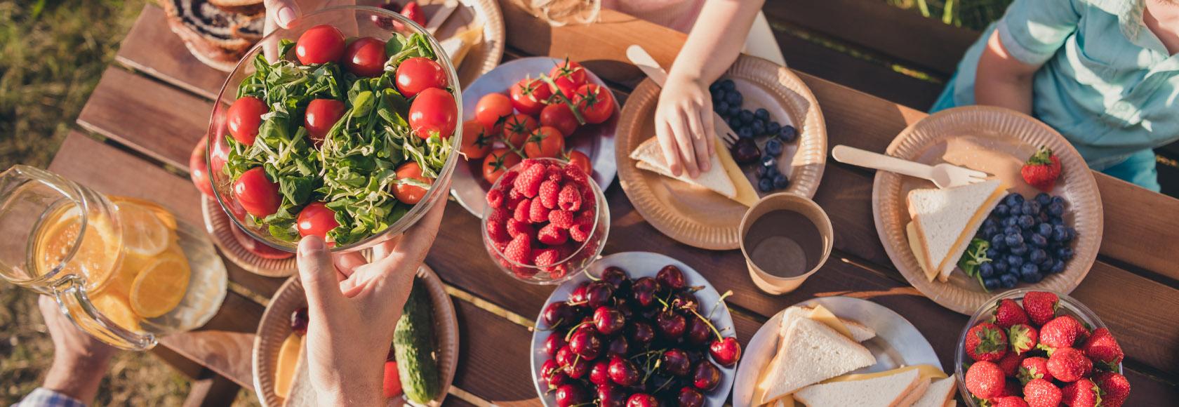 Widok z góry na stoł, na którym są na talerzach pomidory, maliny, czereśnie, truskawki, kanapki z serem oraz roszponka.