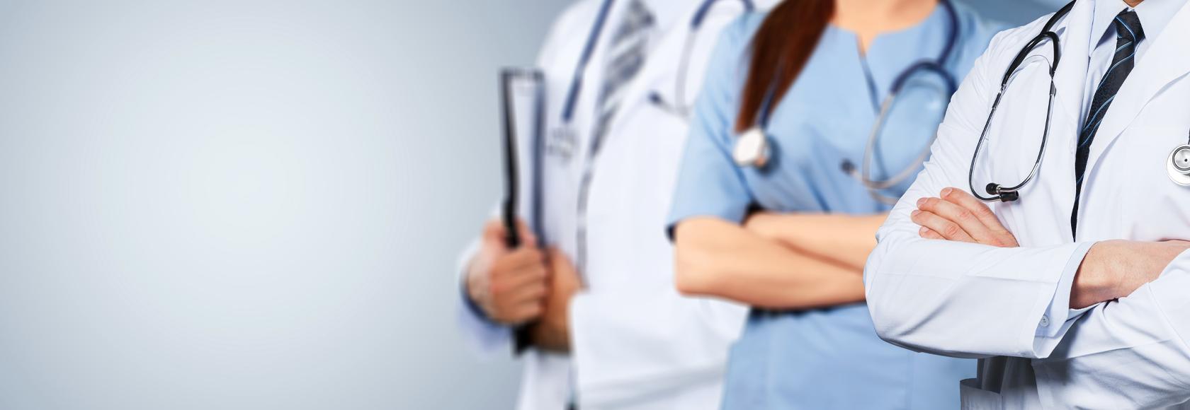 Trójka lekarzy z stetoskopami na szyi stoi w rzędzie. Zbliżenie na ich ręce założone na siebie.