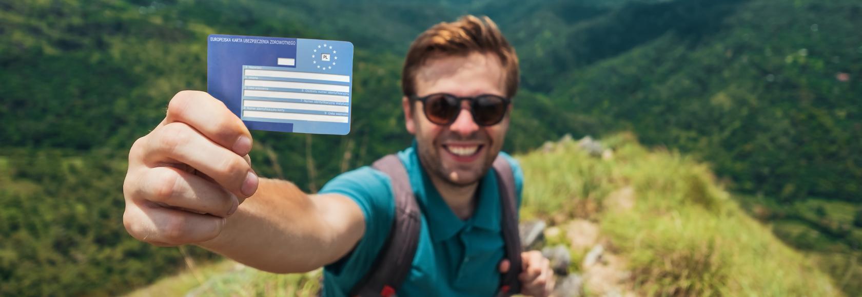 Turysta pokazujący kartę EKUZ. W tle góry